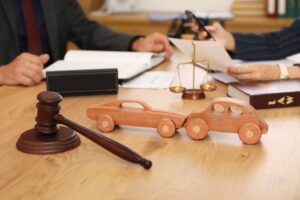 Closeup of wooden car models and a judge's gavel on a lawyer's desk during a meeting in an office setting.